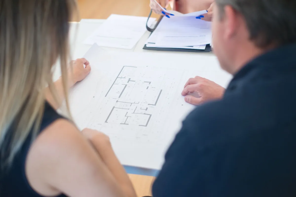 Two people at a desk reviewing an architectural floor plan