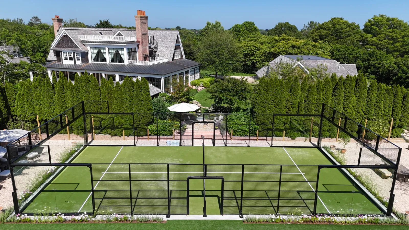 Residential padel court with green turf behind a shingle-style house